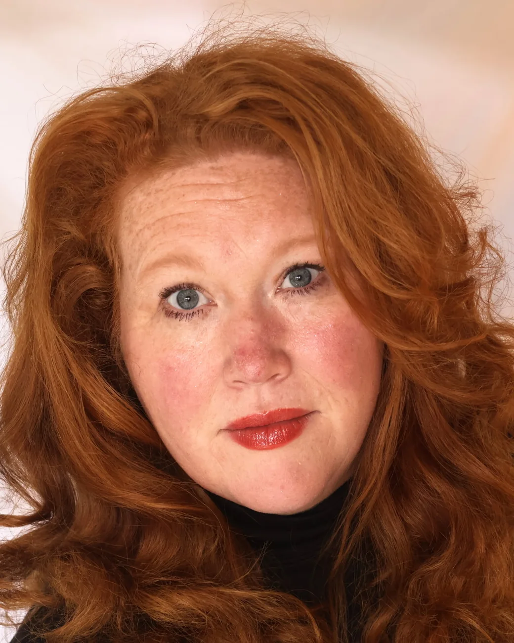 Dawnmarie Neet, with long red hair and a black turtleneck, looking at the camera